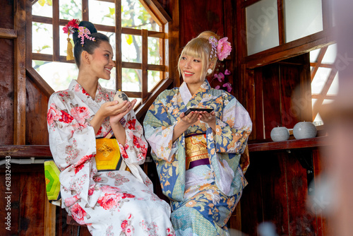 Two Asian women wear japanese style dress sit and enjoy in small shop and also hold small gift and look to each other with happiness.