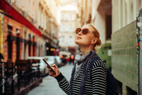 A young female traveler walks through the streets of a European city using a smartphone. Blonde in dark glasses and with a backpack, independent walks to the sights photo