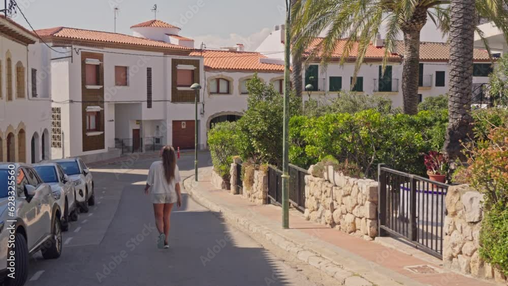A woman strolling alongside parked cars on a scenic street in Terragona A woman strolling alongside parked cars on a scenic street in Terragona