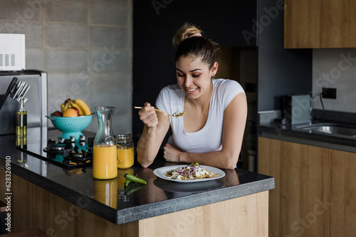 latin woman eating mexican chilaquiles for breakfast in morning in kitchen at home in Mexico, hispanic female in Latin America