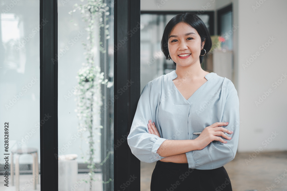 Happy relaxed confident young businesswoman standing with folded arms in a spacious office looking at the camera with a warm friendly smile Happy relaxed confident young businesswoman standing with folded arms in a spacious office looking at the camera with a warm friendly smile