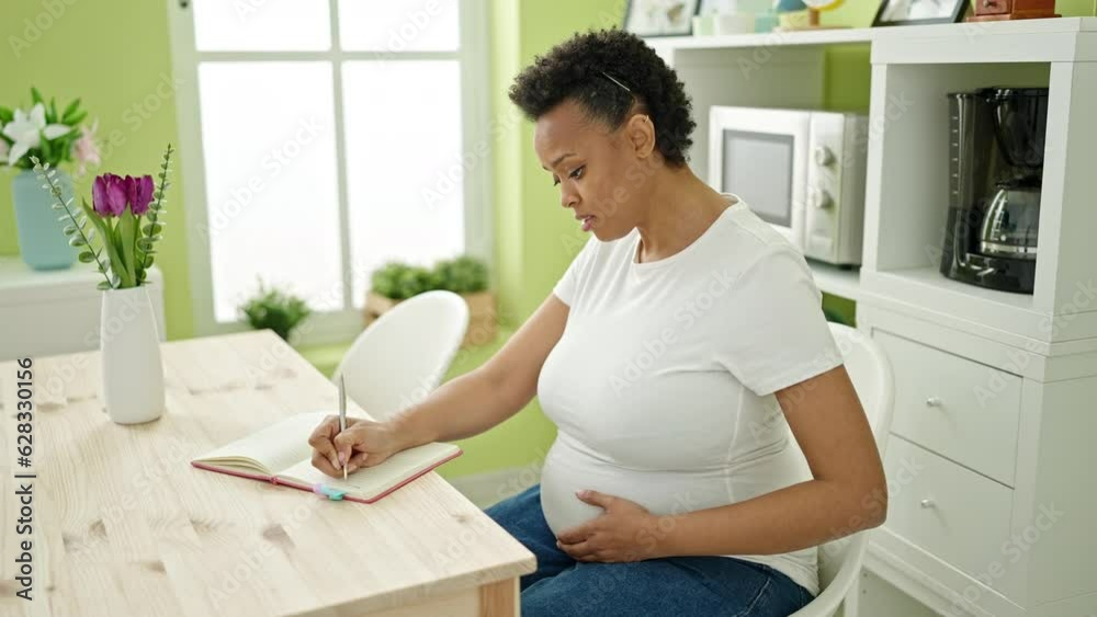 Young pregnant woman writing on notebook feeling baby kick at dinning room Young pregnant woman writing on notebook feeling baby kick at dinning room