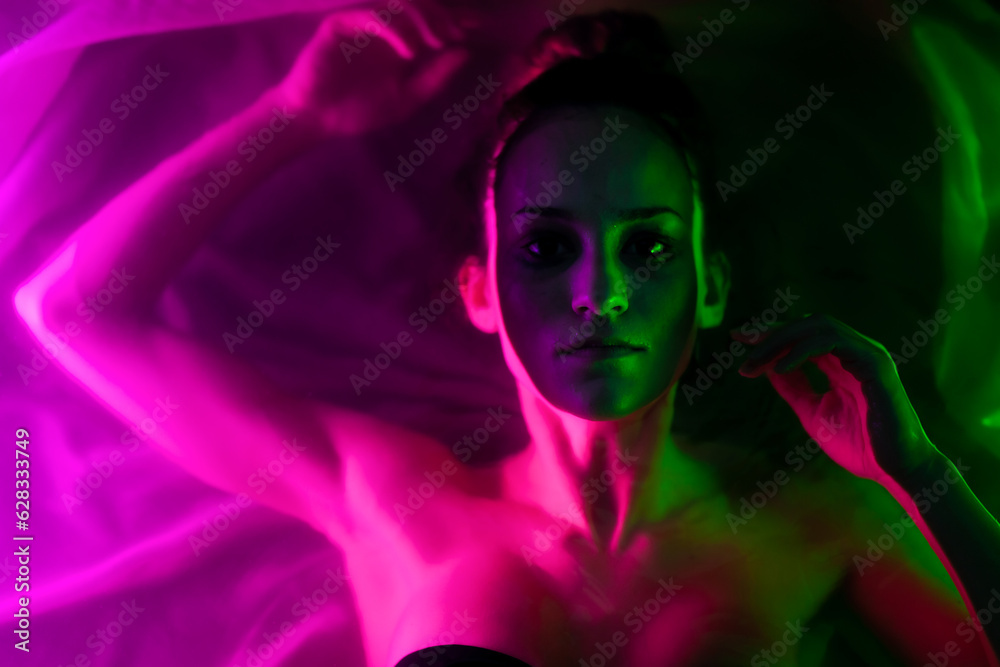 Beautiful wet girl in bikini lying in water portrait. Sidelit with neon lights..