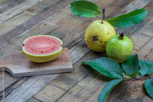 Fresh red guava with green leaves on wooden background. Texture of wood and guava leaves.