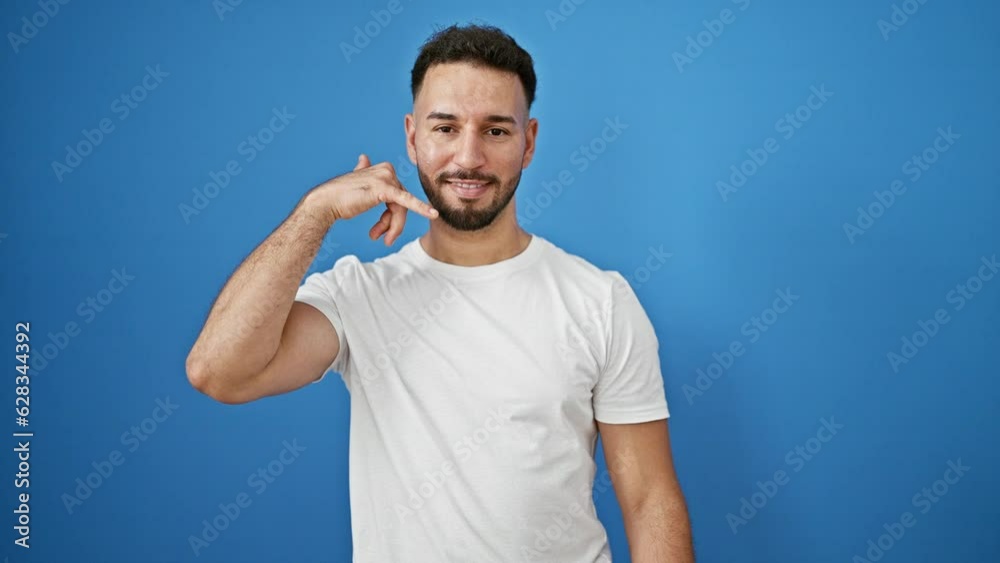 Young arab man smiling confident doing telephone gesture with hand over isolated blue background