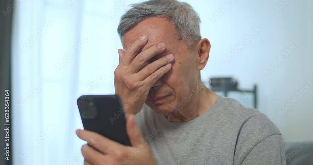 Asian senior man holding phone at home. He suffering from headache at home. healthcare, pain, stress, age and people concept. Asian senior man holding phone at home. He suffering from headache at home. healthcare, pain, stress, age and people concept.