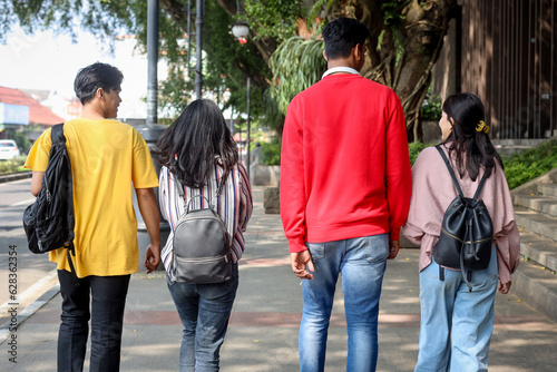 Rear view of happy college students walking together near campus building