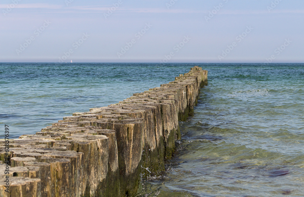 Fototapeta premium Wooden breakwater in the blue turquoise Baltic Sea with horizon and calm water. Diagonal.