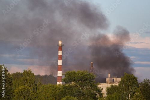 Soft focus. Shooting with a telephoto lens from a distance. Black smoke from a fire on the background of industrial buildings.