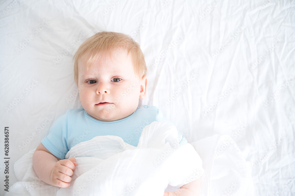 A baby with blonde hair smiling laying on a white bed. top view A baby with blonde hair smiling laying on a white bed. top view