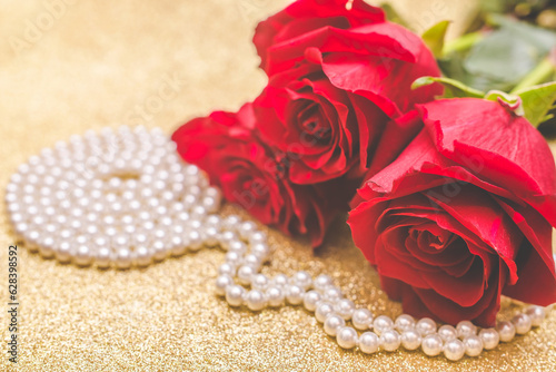 Red rose and pearl necklace on a shiny gold background 
