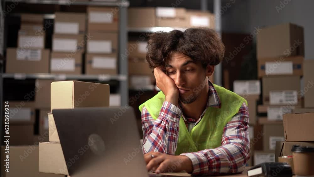 Young tired worker sitting in warehouse with laptop computer and taking a nap. Young tired worker sitting in warehouse with laptop computer and taking a nap.