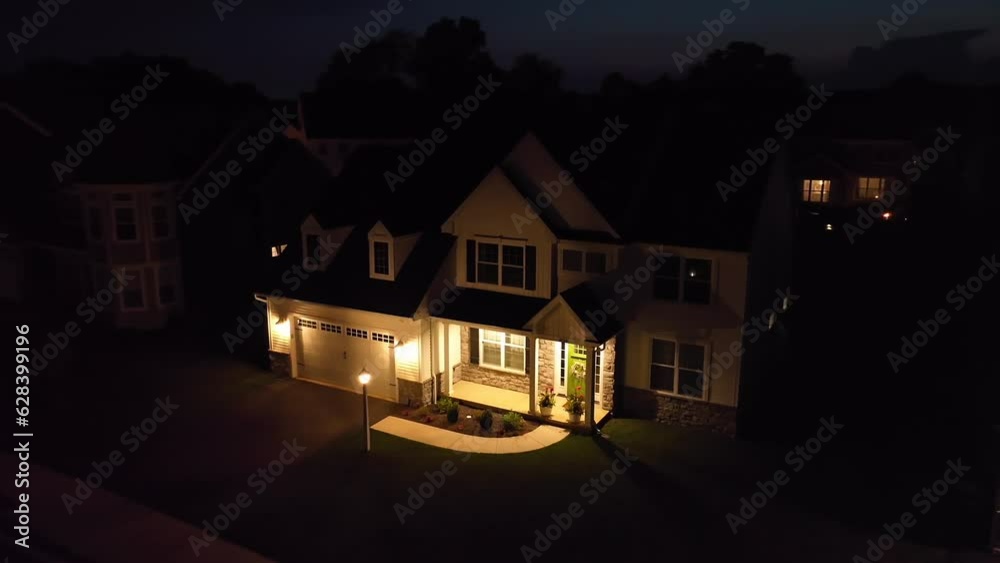Upscale American home at night. Dark scene with bright lights on porch and garage. Aerial establishing shot of USA house and neighborhood. Upscale American home at night. Dark scene with bright lights on porch and garage. Aerial establishing shot of USA house and neighborhood.