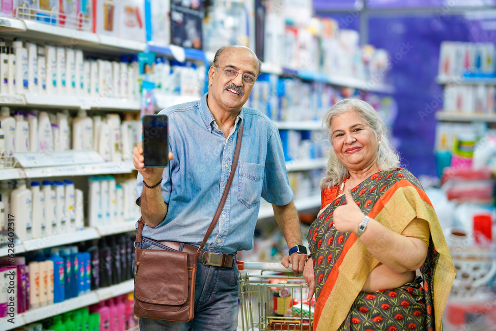 Senior man showing smartphone with his wife at grocery shop. Senior man showing smartphone with his wife at grocery shop.