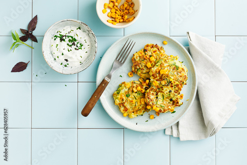 Zucchini and corn fritters with sour cream and herbs. Top view, flat lay. photo