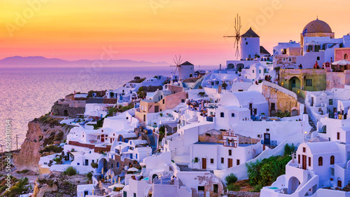 Sunset with white churches an blue domes by the ocean of Oia Santorini Greece.