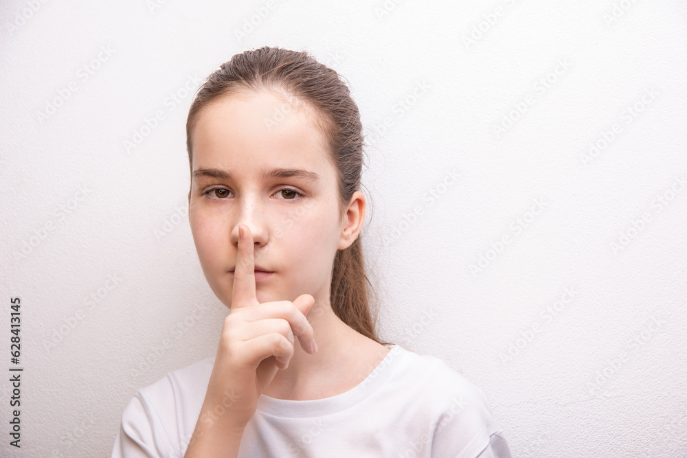 dont speak teen girl show gesture silence hush sign, wearing white T-shirt over white paint wall dont speak teen girl show gesture silence hush sign, wearing white T-shirt over white paint wall