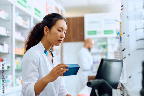 Chinese female pharmacist works on computer in drugstore.