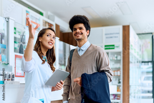 Happy pharmacists assists her male customer in pharmacy.