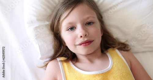 Beautiful little girl takes selfie and falls on bed. Portrait of cute baby girl on pillow photo