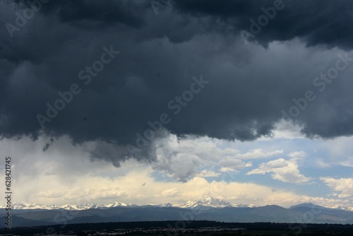 ominous afternoon storm clouds in early summer over the snow-capped front range of the colorado rocky mountains as seen from Broomfield, colorado