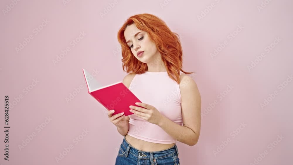 Young redhead woman reading book with serious expression over isolated pink background Young redhead woman reading book with serious expression over isolated pink background