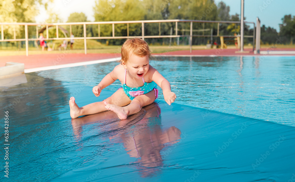 Little girl is playing in the pool. Happy child outside in the water. Pretty girl in a blue bathing suit.
