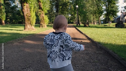 Baby takes first steps. Baby boy running in the park. Happy childish dream concept in park. Single baby child walking single along the path in the park. Kid run in nature in park 4k