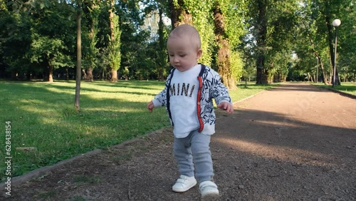 Baby takes first steps. Baby boy running in the park. Happy childish dream concept in park. Single baby child walking single along the path in the park. Kid run in nature in park 4k