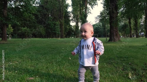 Baby takes first steps. Baby boy running in the park. Happy baby takes first steps in nature. Toddler walks on grass in park. Baby learns to walk. Happy family kid concept 4k