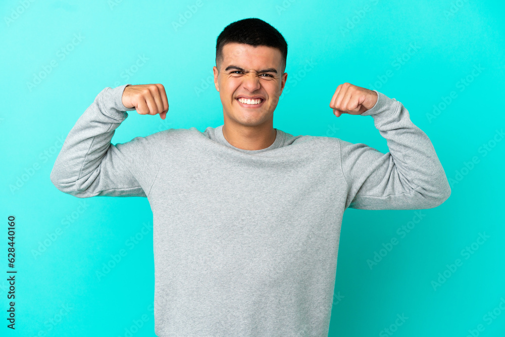 Young handsome man over isolated blue background doing strong gesture Young handsome man over isolated blue background doing strong gesture