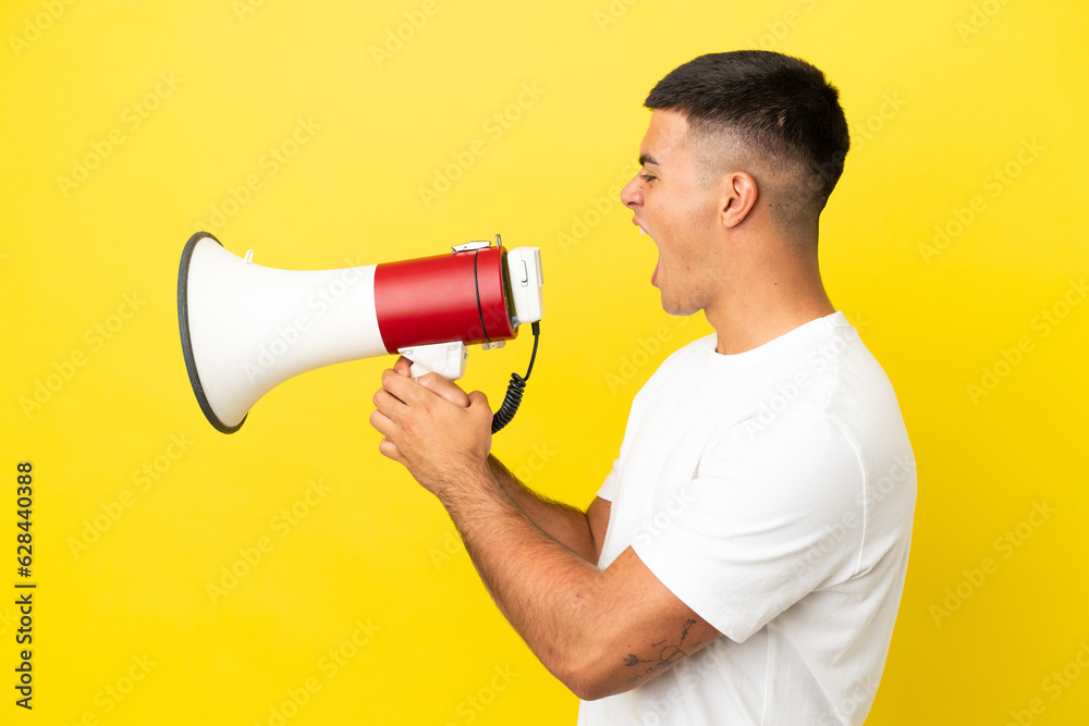 Young handsome man over isolated yellow background shouting through a megaphone to announce something in lateral position Young handsome man over isolated yellow background shouting through a megaphone to announce something in lateral position