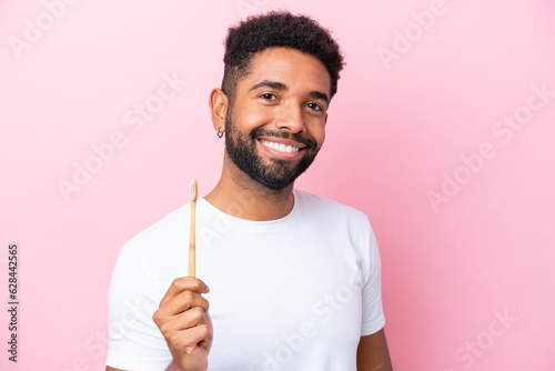 Young Brazilian man brushing teeth isolated on pink background smiling a lot