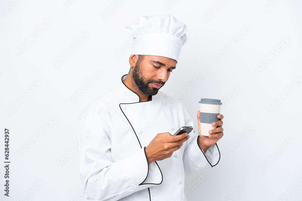 Young Brazilian chef man isolated on white background holding coffee to take away and a mobile Young Brazilian chef man isolated on white background holding coffee to take away and a mobile
