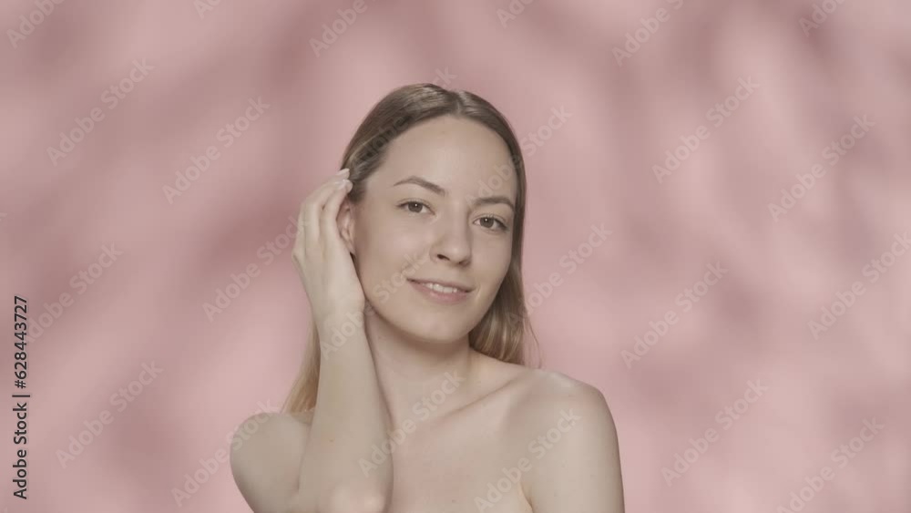 A woman touches the skin under her eyes, runs her hand along her slender neck. A seminude woman in the studio on a pink background close up. HDR BT2020 HLG Material. A woman touches the skin under her eyes, runs her hand along her slender neck. A seminude woman in the studio on a pink background close up. HDR BT2020 HLG Material.