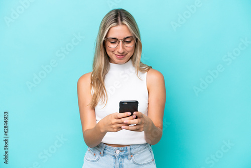 Young caucasian woman isolated on blue background sending a message with the mobile