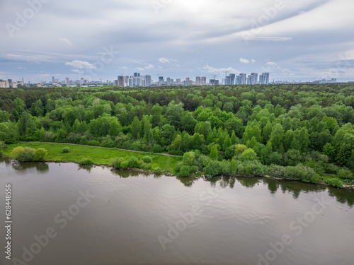 Big lake with green shores in bright sun light and city on horizon, aerial landscape. Recreation concept. Aerial view