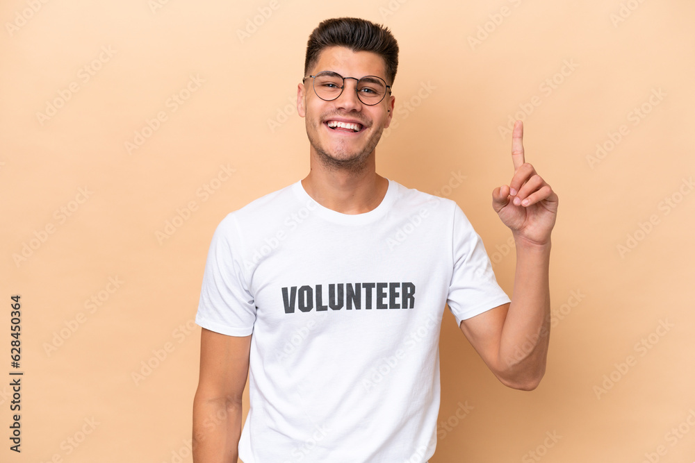 Young volunteer caucasian man isolated on beige background showing and lifting a finger in sign of the best Young volunteer caucasian man isolated on beige background showing and lifting a finger in sign of the best