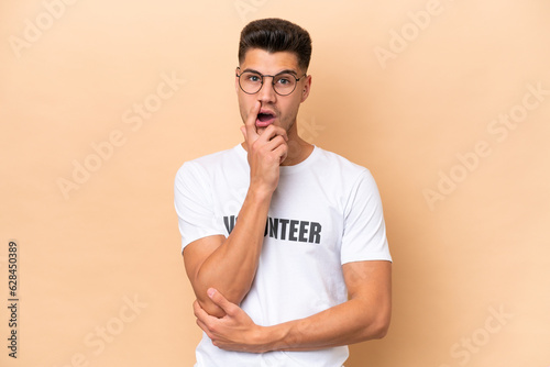 Young volunteer caucasian man isolated on beige background surprised and shocked while looking right