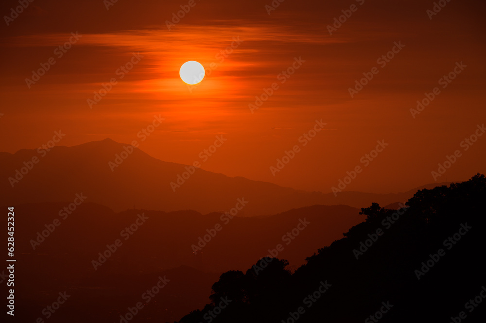 The orange-red sunset is covered by clouds as it moves towards the horizon. View of the urban landscape from Dajianshan Mountain, New Taipei City.