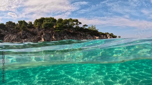 Crystal clear sea water in Sitonia, Halkidiki, Greece. Shot from border of air and water with dome. Half underwater slow-motion view of sandy beach bottom and rock with trees