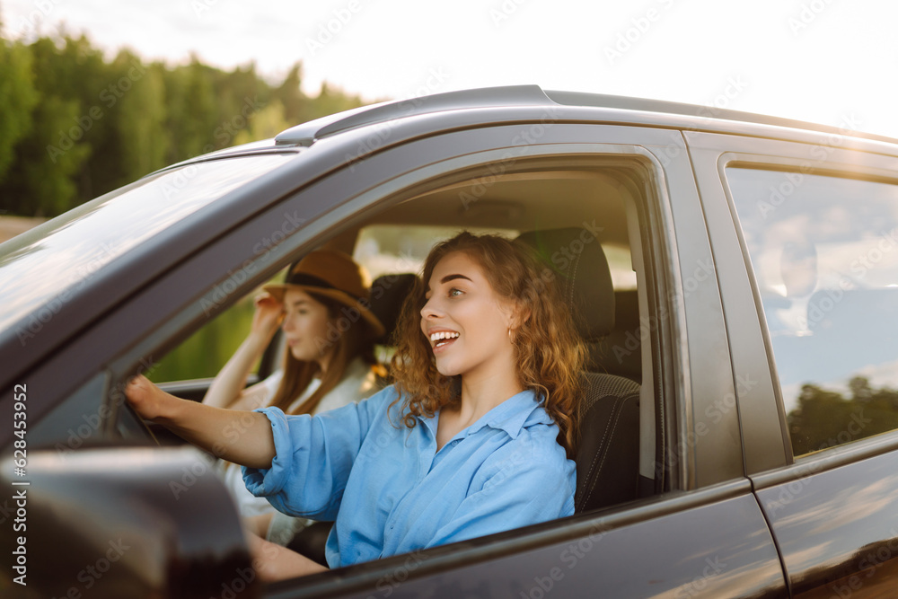 Naklejka premium Portrait of two young women on a car trip having fun, smiling, chatting together, enjoying nature. Active lifestyle, travel, tourism, nature.
