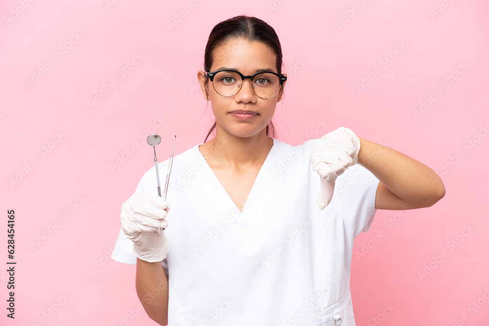 Dentist Colombian woman isolated on pink background showing thumb down with negative expression Dentist Colombian woman isolated on pink background showing thumb down with negative expression