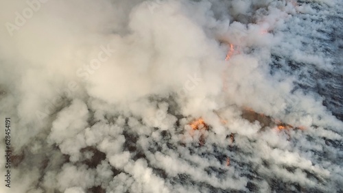 Flying over wildfire and plumes of smoke. Natural disaster due to extreme heat and climate change. Aerial view of big smoke clouds and fire on the field. Grass fire aerial shot. Big smoke clouds and photo