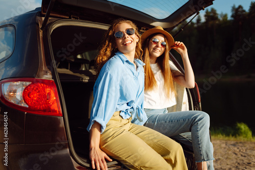 Portrait of two young women on a car trip having fun, smiling, chatting together, enjoying nature. Active lifestyle, travel, tourism, nature. © maxbelchenko