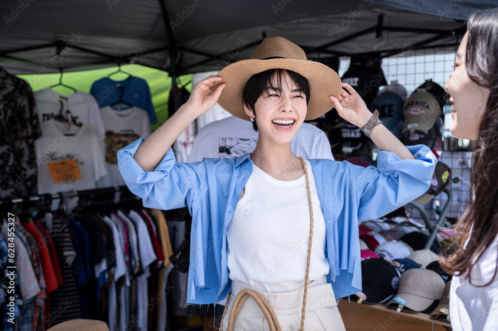 A young Asian woman and her friend happily try on hats in an outdoor clothing shop.
A young Asian woman and her friend happily try on hats in an outdoor clothing shop.