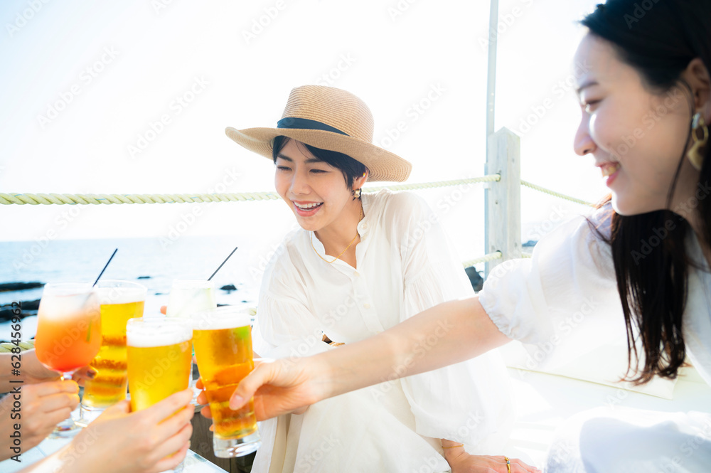 Young Asian girls toasting drinks at a seaside restaurant, smiling joyfully Young Asian girls toasting drinks at a seaside restaurant, smiling joyfully
