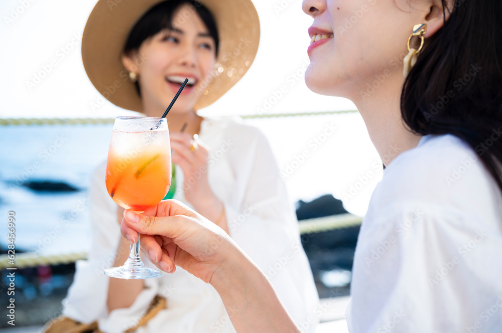 Young Asian girls toasting drinks at a seaside restaurant, smiling joyfully Young Asian girls toasting drinks at a seaside restaurant, smiling joyfully