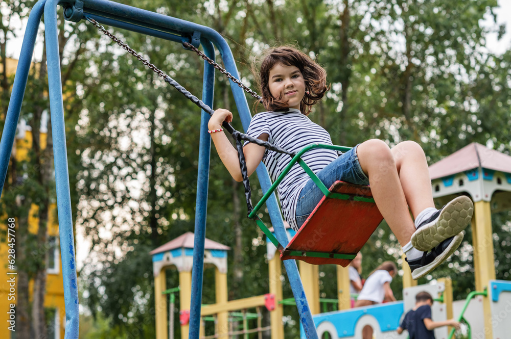 joyful smiling teenager girl 11 years old rides on a swing on the playground looks at the camera close-up. High quality photo