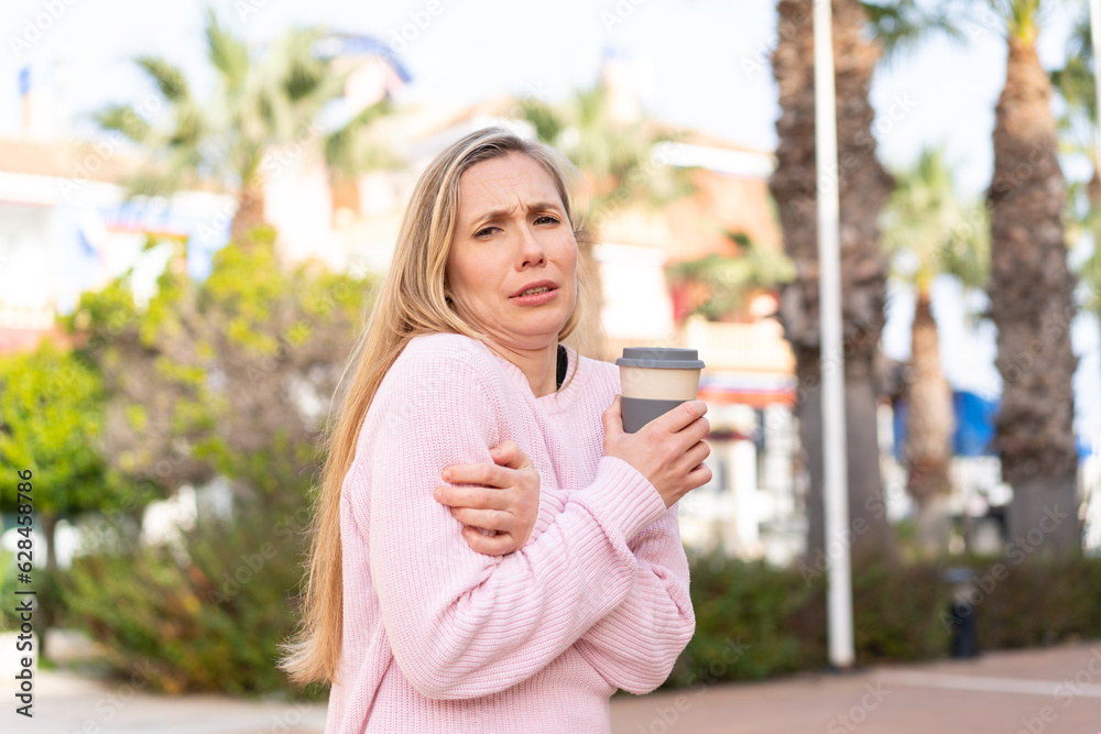 Young blonde woman holding a take away coffee at outdoors Young blonde woman holding a take away coffee at outdoors